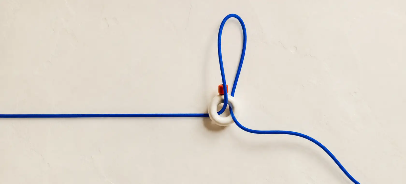 Un único cordón azul forma un lazo a través de una anilla blanca sobre pared de cal